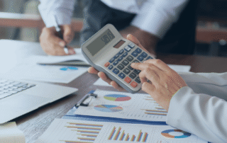 A pair of hands using a calculator while another writes on paper.