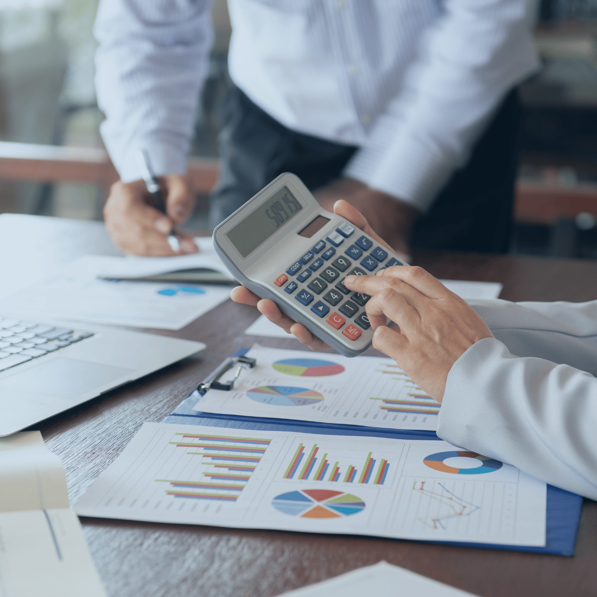 A pair of hands using a calculator while another writes on paper.