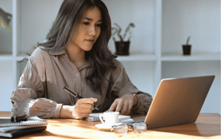 Business professional taking notes while working on a laptop at her desk.